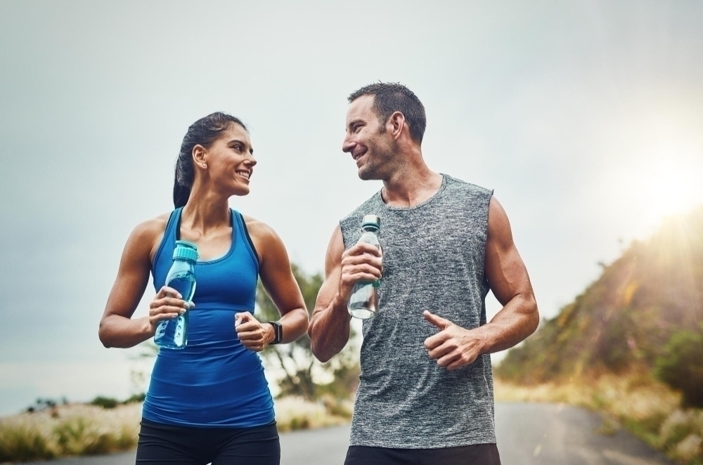 Fitness runner or happy couple drinking water on break to hydrate or relax for healthy energy in exercise Tired people and thirsty athletes with liquid or hydration in marathon training or workout