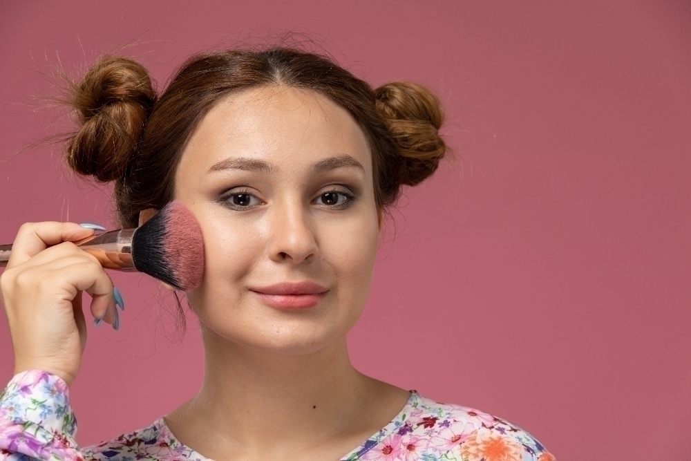 Front close view young female in flower designed shirt doing make up on the pink background
