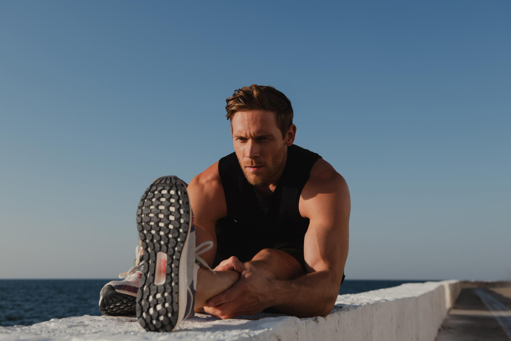 Handsome young male athlete in sports clothing doing stretching exercises before jogging seaside