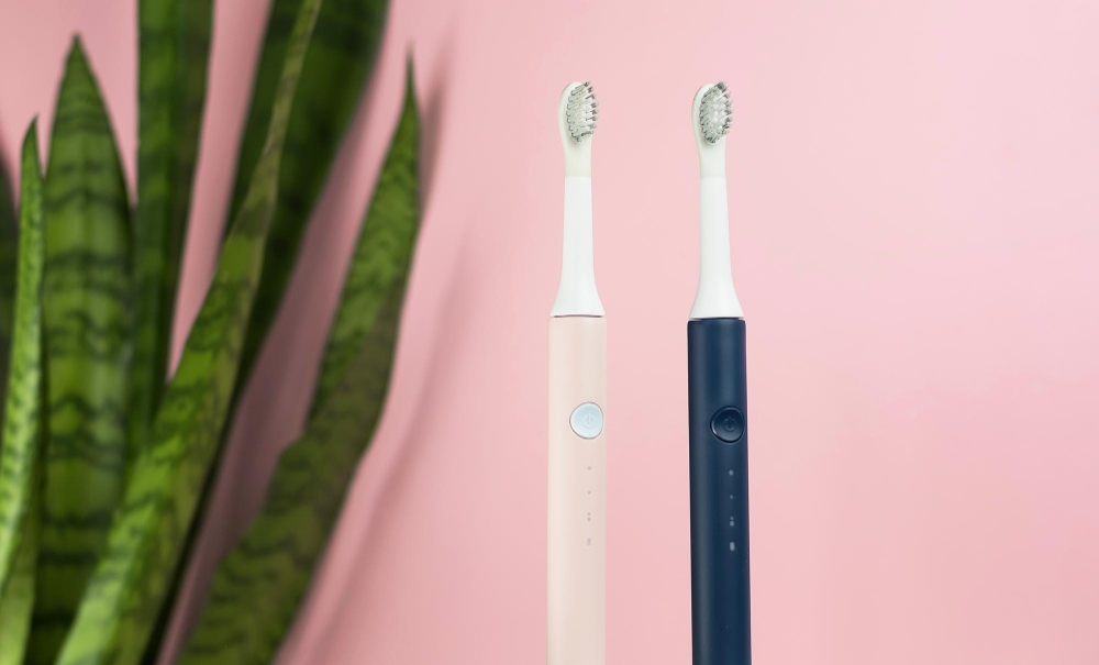 New modern ultrasonic toothbrushes. Dental care supplies with green leaves on pink pastel background. Oral hygiene gum health healthy teeth. Dental products Ultrasonic vibration toothbrush.
