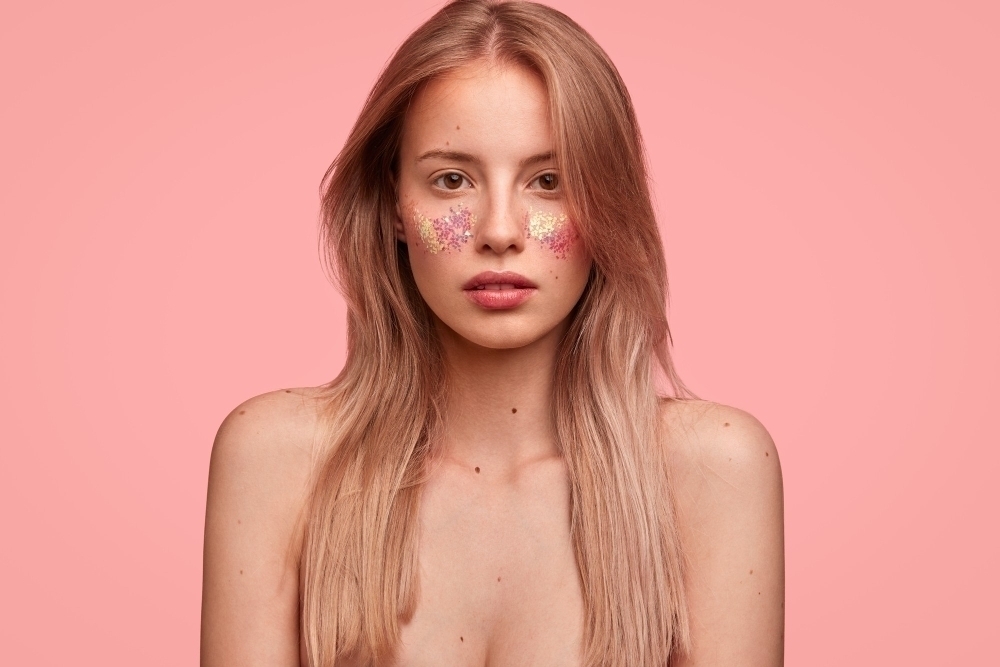 Portrait of young blonde woman with glitter on face and stylish hat