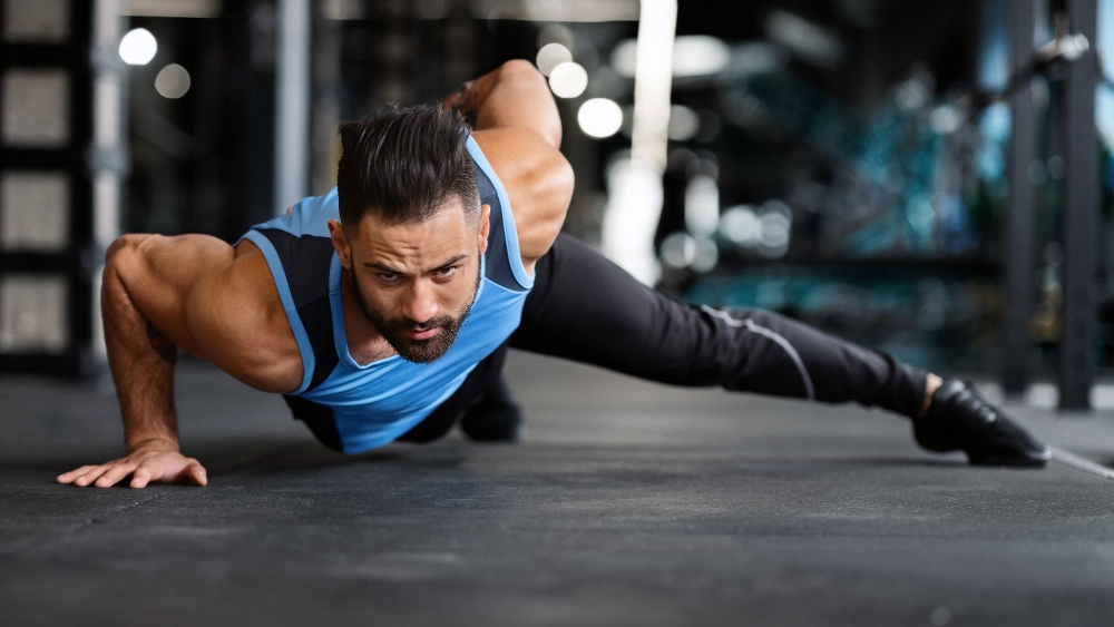 Strength exercise muscular man doing push ups on on hands in gym panorama